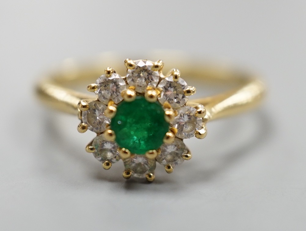 A modern 18ct gold, emerald and diamond set circular cluster ring, size M, gross weight 3 grams.
